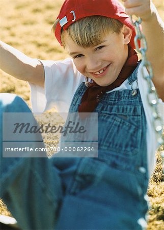 Portrait of Boy Wearing Overalls And Hat, Sitting on Swing - Stock Photo - 700-00062264em