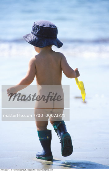 Back View of Nude Child Walking On Beach Carrying Shovel
