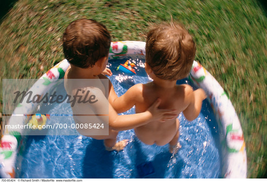 Back View of Two Nude Children Standing in Inflatable Swimming Pool