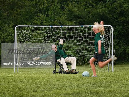 Soccer jeu de fille (10-11) avec grand-père en fauteuil roulant comme gardien de but