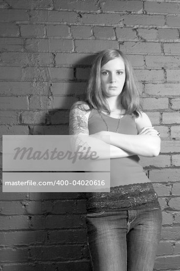 A young female with full arm tattoo leaning up against a black brick wall