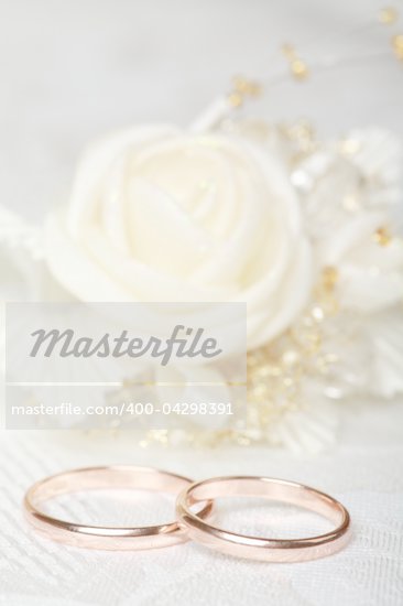 Gold wedding rings and satin rose flower on lace background