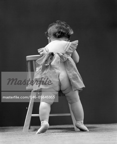 1940s BACK END VIEW OF NUDE GIRL BABY WEARING PINAFORE APRON Stock Photo 