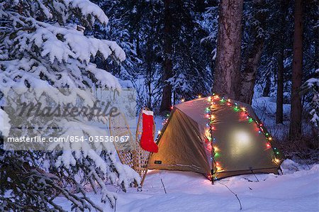 tent is set up in the woods with Christmas lights and stocking near ...