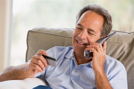 Man indoors using telephone and looking at credit card smiling Stock Photo - Budget Royalty-Free & Subscription, Code: 400-04046278
