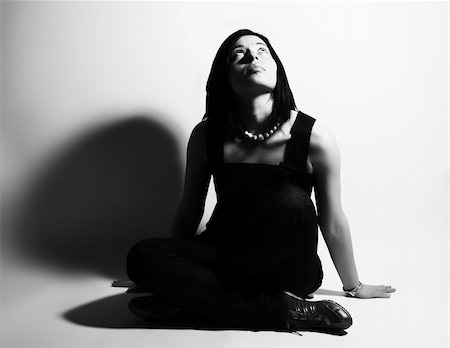 spreading hair of girl image picture - A black and white high-key portrait about an attractive trendy girl with black hair who is sitting, she is spreading her arms on ground and she is dreaming about something. She is wearing a black dress, blue jeans and a white necklace. Stock Photo - Budget Royalty-Free & Subscription, Code: 400-04060648