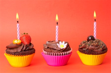 simsearch:400-04764403,k - Three miniature chocolate cupcakes with icing, decorations and birthday candles on red background Stock Photo - Budget Royalty-Free & Subscription, Code: 400-04106988