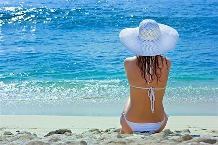 simsearch:400-04127663,k - Beautiful brunette with long hair in white hat and swimsuit sits on the sand ocean beach on Bali in Indonesia Foto de stock - Super Valor sin royalties y Suscripción, Código: 400-04127676