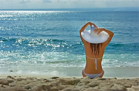 simsearch:400-04127663,k - Beautiful brunette with long hair in white hat and swimsuit sits on the sand ocean beach on Bali in Indonesia Foto de stock - Super Valor sin royalties y Suscripción, Código: 400-04127678