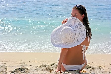 simsearch:400-04127663,k - Beautiful brunette with long hair in white hat and swimsuit sits on the sand ocean beach on Bali in Indonesia Foto de stock - Super Valor sin royalties y Suscripción, Código: 400-04127680