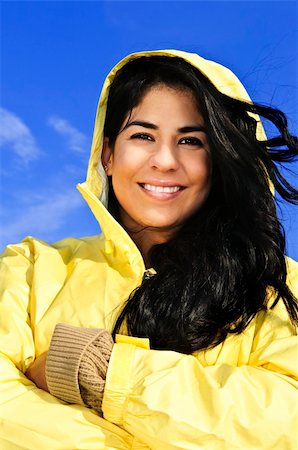Portrait of beautiful smiling brunette girl wearing yellow raincoat against blue sky Stock Photo - Budget Royalty-Free & Subscription, Code: 400-04121691