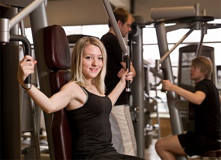 simsearch:400-04148009,k - Girl using an exercise machine at a health club with two men in the background Photographie de stock - Aubaine LD & Abonnement, Code: 400-04147994