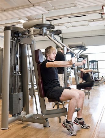 simsearch:400-04148009,k - Young man using an exercise machine at a health club with a girl and a boy in the background Photographie de stock - Aubaine LD & Abonnement, Code: 400-04147995