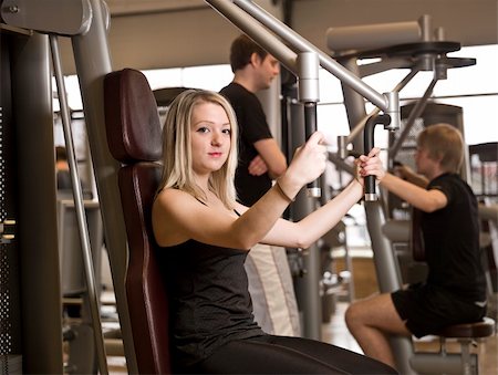 simsearch:400-04148009,k - Girl using an exercise machine at a health club with two men in the background Photographie de stock - Aubaine LD & Abonnement, Code: 400-04147990