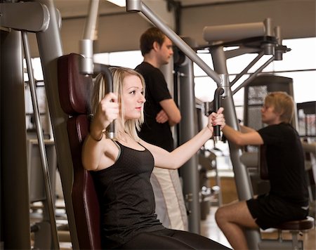 simsearch:400-04148009,k - Girl using an exercise machine at a health club with two men in the background Photographie de stock - Aubaine LD & Abonnement, Code: 400-04147992