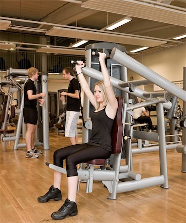 simsearch:400-04148009,k - Girl using an exercise machine at a health club with two men in the background Photographie de stock - Aubaine LD & Abonnement, Code: 400-04148003