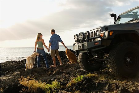 Rear view of a man and woman holding hands and relaxing with their dogs at a beach with the edge of an SUV visible in the foreground. Horizontal format. Stock Photo - Budget Royalty-Free & Subscription, Code: 400-04169275