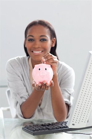 savings and loan security - Smiling ethnic businesswoman saving money in a piggybank at her desk Stock Photo - Budget Royalty-Free & Subscription, Code: 400-04188684