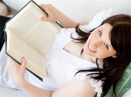 simsearch:400-04418460,k - Bright brunette teenager holding a book smiling at the camera in the living room Stock Photo - Budget Royalty-Free & Subscription, Code: 400-04206738