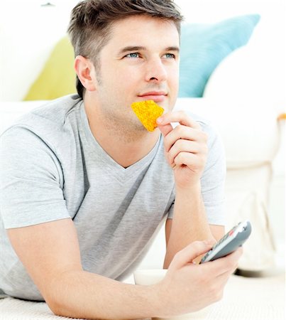 simsearch:400-04210845,k - Jolly young man holding a remote eating crisps lying on the flloor in the living-room Stock Photo - Budget Royalty-Free & Subscription, Code: 400-04209884