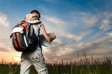 beautiful young woman with backpack and map in hand standing outside in the field with her back to camera. Sunset cloudy blue sky in background and green grass in foreground Photographie de stock - Aubaine LD & Abonnement, Code: 400-04200702