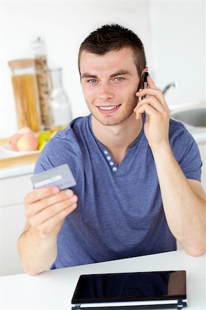 simsearch:400-04212823,k - Attractive young man talking on phone holding a card looking at the camera in the kitchen Stock Photo - Budget Royalty-Free & Subscription, Code: 400-04210808