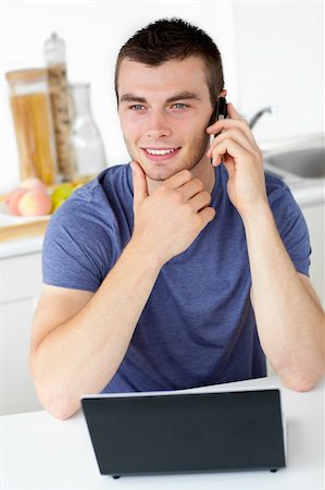 simsearch:400-04212823,k - Smiling man talking on phone using his laptop in the kitchen at home Stock Photo - Budget Royalty-Free & Subscription, Code: 400-04210812