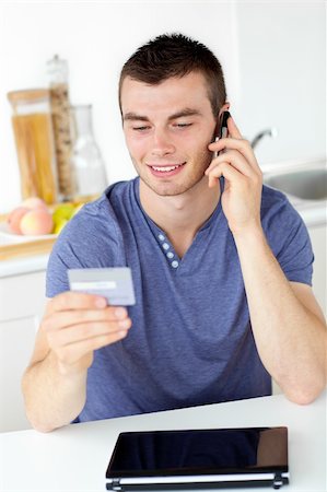 simsearch:400-04212823,k - Attractive young man talking on phone holding a card in the kitchen at home Stock Photo - Budget Royalty-Free & Subscription, Code: 400-04212833