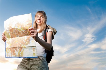 beautiful young woman with backpack and map in hands standing outside in the field and looking away from map. Blue cloudy sky in background. Stock Photo - Budget Royalty-Free & Subscription, Code: 400-04227624