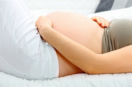 Pregnant woman lying on sofa at home and holding her belly. Close-up. Stock Photo - Budget Royalty-Free & Subscription, Code: 400-04277511