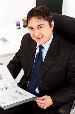 simsearch:400-05748170,k - Smiling modern businessman sitting at office desk and working  with financial documents Stock Photo - Budget Royalty-Free & Subscription, Code: 400-04305087