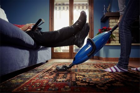 caucasian heterosexual couple, with woman doing chores using vacuum cleaner on carpet and lazy man on sofa with tablet pc. Horizontal shape, low angle view Stock Photo - Budget Royalty-Free & Subscription, Code: 400-04300669