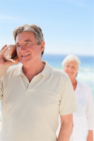 elderly women in bathing suits& - Man listening his shell with his wife behind him Stock Photo - Budget Royalty-Free & Subscription, Code: 400-04331792