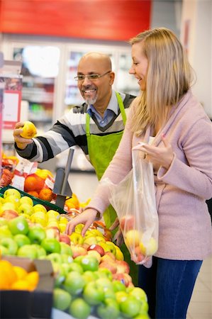 Happy young woman buying fruits with shop assistant in the background Stock Photo - Budget Royalty-Free & Subscription, Code: 400-04389402