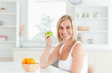 Young blonde woman holding a green apple smiling into the camera in the kitchen Stock Photo - Budget Royalty-Free & Subscription, Code: 400-04417535