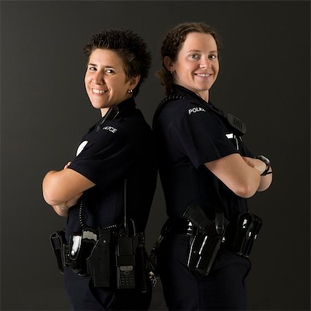 female police officer happy - Portrait of two mid adult Caucasian policewomen standing back to back looking over their shoulders smiling at viewer. Photographie de stock - Aubaine LD & Abonnement, Code: 400-04468905