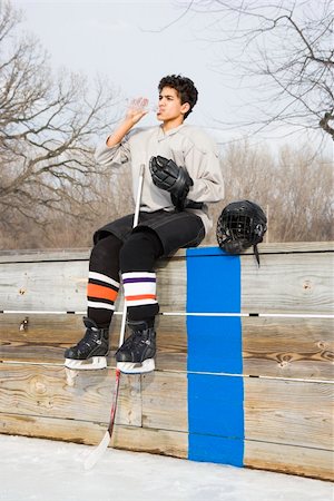 Boy in ice hockey uniform holding hockey stick sitting on sidelines drinking water. Stock Photo - Budget Royalty-Free & Subscription, Code: 400-04471036