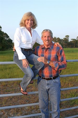 A good looking mature couple on a farm.  The wife is sitting on the fence with her husband standing beside her. Stock Photo - Budget Royalty-Free & Subscription, Code: 400-04486149