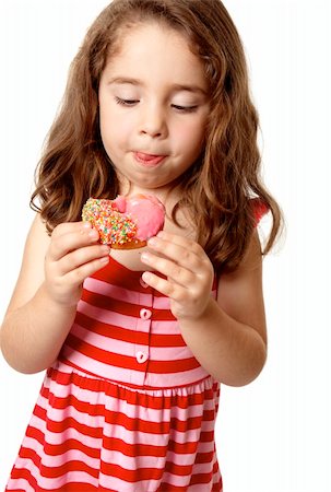Young girl eating a delicious pink iced doughnut.  She is looking down at it  and licking her lips. Foto de stock - Super Valor sin royalties y Suscripción, Código: 400-04583663