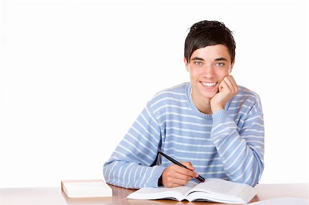 simsearch:400-04704759,k - Young student is sitting on desk with open book and learns for his exams. He looks smiling into camera. Isolated on white. Stock Photo - Budget Royalty-Free & Subscription, Code: 400-04680533