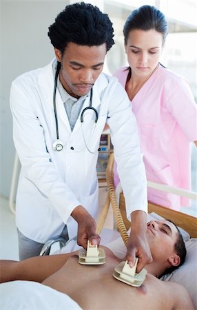 Ethnic doctor using a defibrillator on a patient in a hospital Stock Photo - Budget Royalty-Free & Subscription, Code: 400-04699423