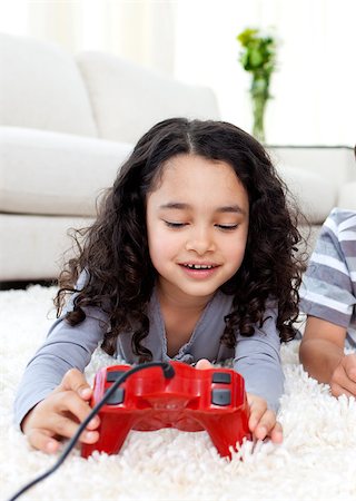 simsearch:400-05751526,k - Cute girl playing video games lying on the floor with her parents in the background Stock Photo - Budget Royalty-Free & Subscription, Code: 400-04691673
