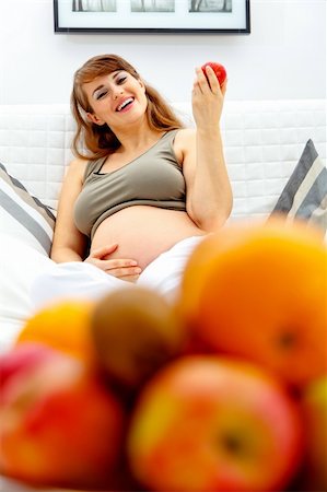 simsearch:400-04817039,k - Smiling  beautiful pregnant woman relaxing on couch at home and  holding fruit in hand Stock Photo - Budget Royalty-Free & Subscription, Code: 400-04755000