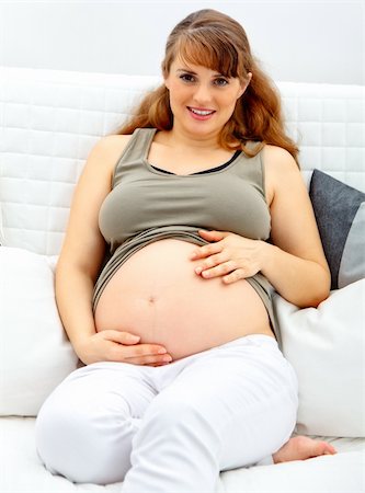 simsearch:400-04817039,k - Smiling beautiful pregnant woman sitting on sofa at home and touching her belly. Stock Photo - Budget Royalty-Free & Subscription, Code: 400-04766942