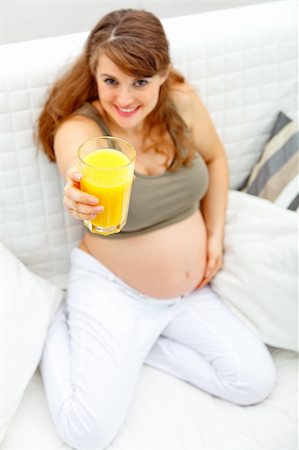 simsearch:400-04817039,k - Smiling beautiful pregnant woman sitting on sofa at home with glass of juice  in hand. Close-up. Stock Photo - Budget Royalty-Free & Subscription, Code: 400-04762785