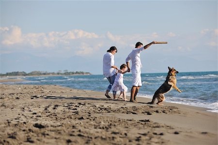 simsearch:400-05309800,k - happy young family in white clothing have fun and play with beautiful dog at vacations on beautiful beach Stock Photo - Budget Royalty-Free & Subscription, Code: 400-04779177