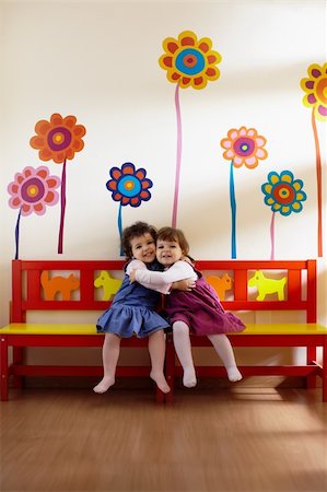 Caucasian and hispanic female preschoolers sitting on bench in kindergarten, playing and smiling. Vertical shape, full length, front view Stock Photo - Budget Royalty-Free & Subscription, Code: 400-04843532