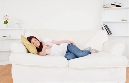 Attractive red-haired female watching tv while lying on a sofa in the living room Stock Photo - Budget Royalty-Free & Subscription, Code: 400-04878765