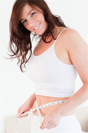 simsearch:400-07219376,k - Attractive brunette woman measuring her belly with a tape measure while standing in her bedroom Stock Photo - Budget Royalty-Free & Subscription, Code: 400-04882156