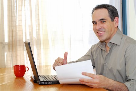 Man sitting at a desk looking at bills and smiling Stock Photo - Budget Royalty-Free & Subscription, Code: 400-04940480